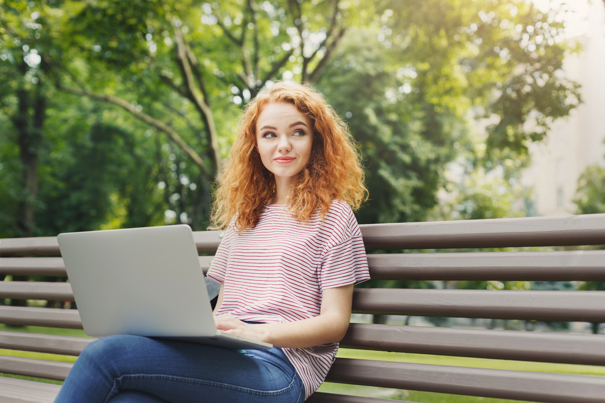 Happy woman is using laptop in the park