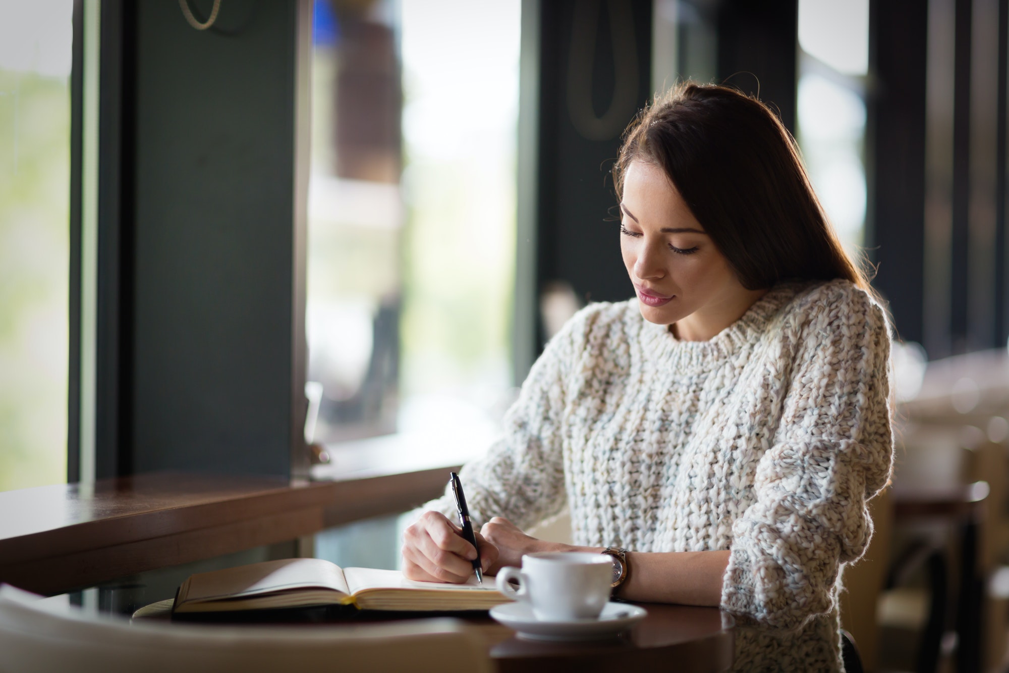 Beautiful woman sitting in restaurant and writing