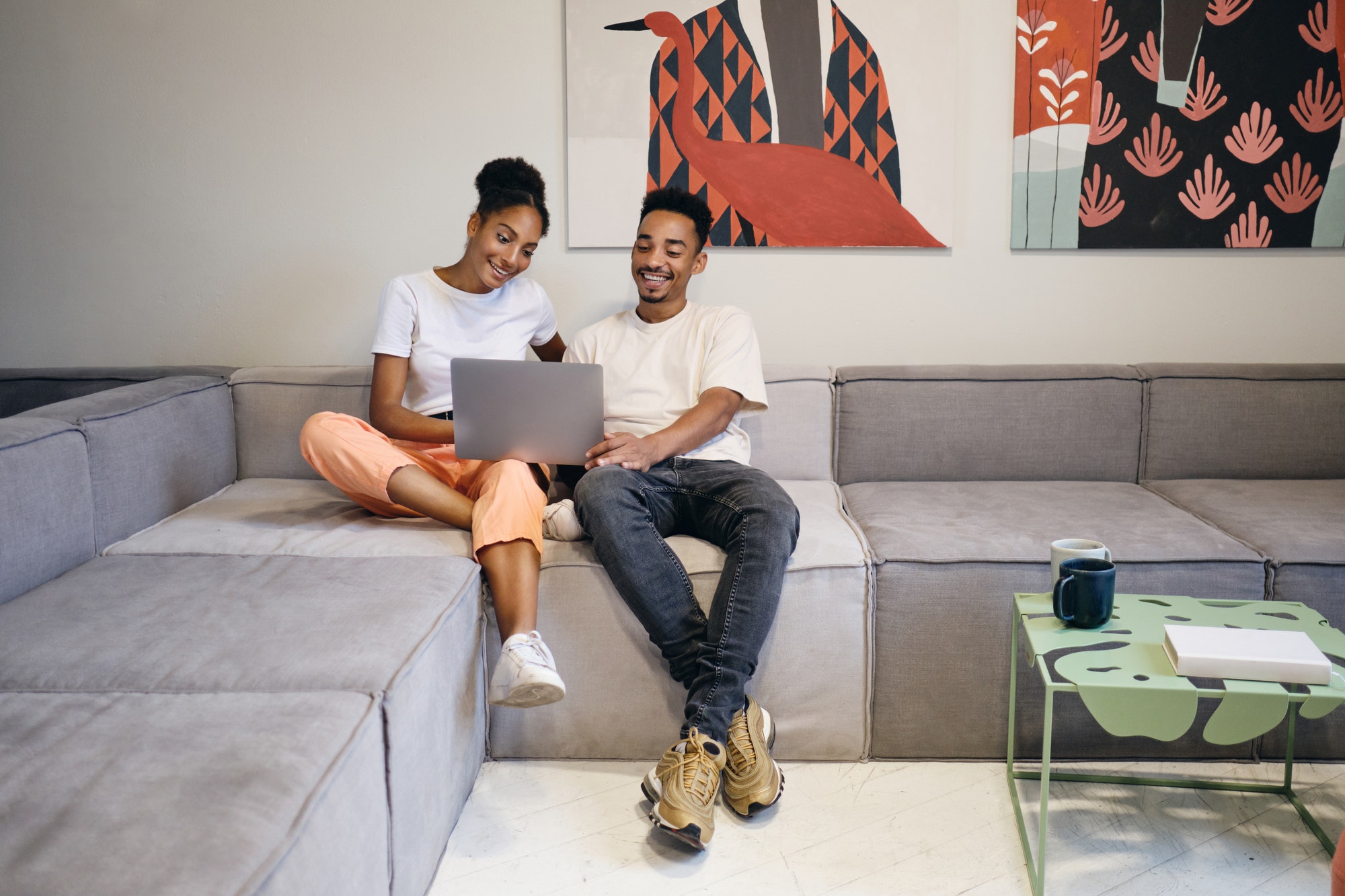 Beautiful casual African American couple happily watching movie on laptop at modern home