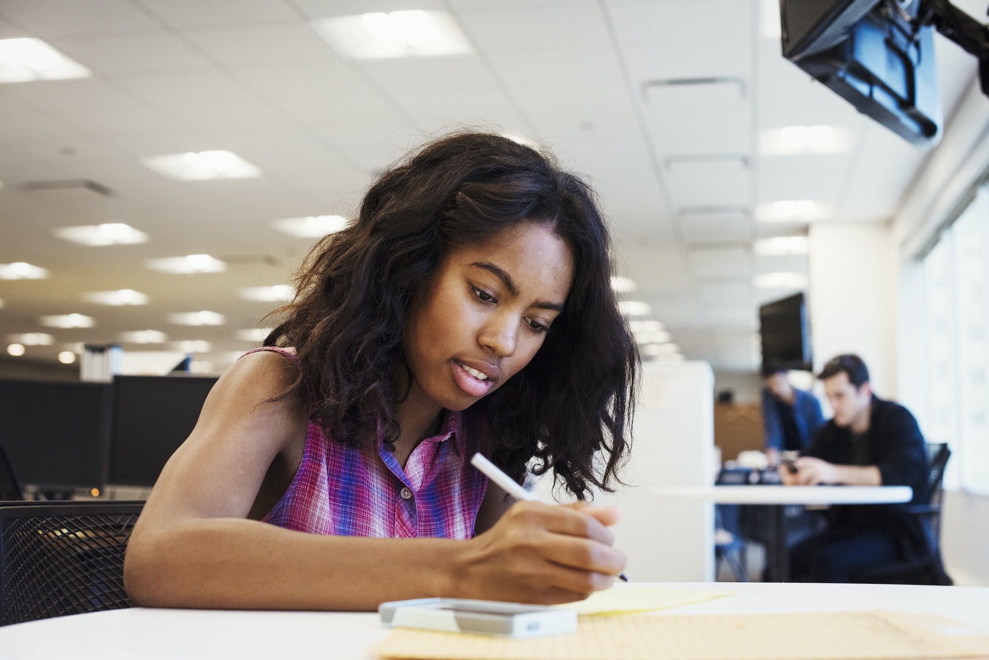 A woman sitting at a table in an office writing.